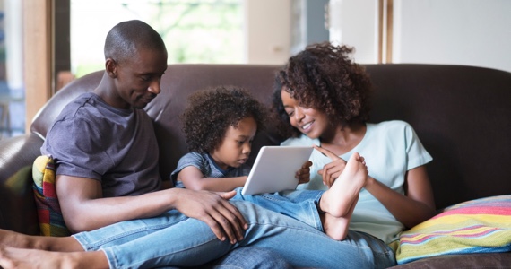 Couple et fillette sur un divan regardent une tablette