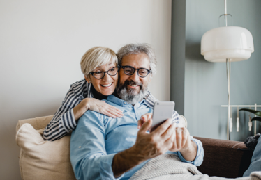 Photo d’un couple de retraités souriants qui regardent ensemble l’écran d’un téléphone cellulaire