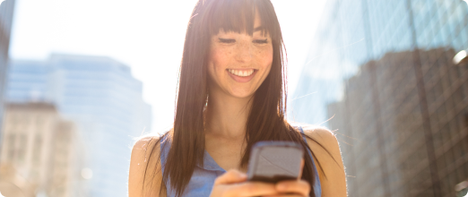 Photo d’une femme regardant son téléphone en souriant avec des gratte-ciels en arrière-plan 