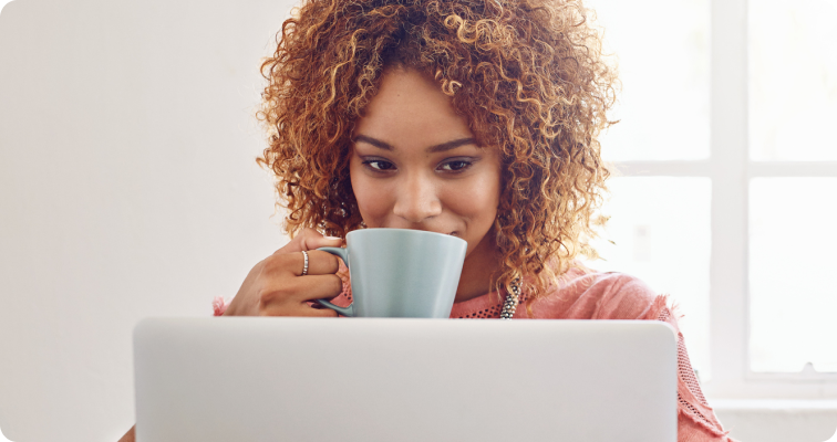 Photo d’une femme qui boit un café devant son ordinateur portable